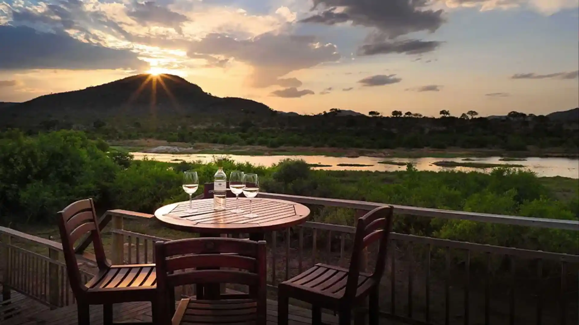 Drinks on a round wood table with cahirs around it at sunset. With a river view in background and sun setting behind a koppie surrounded by bushveld